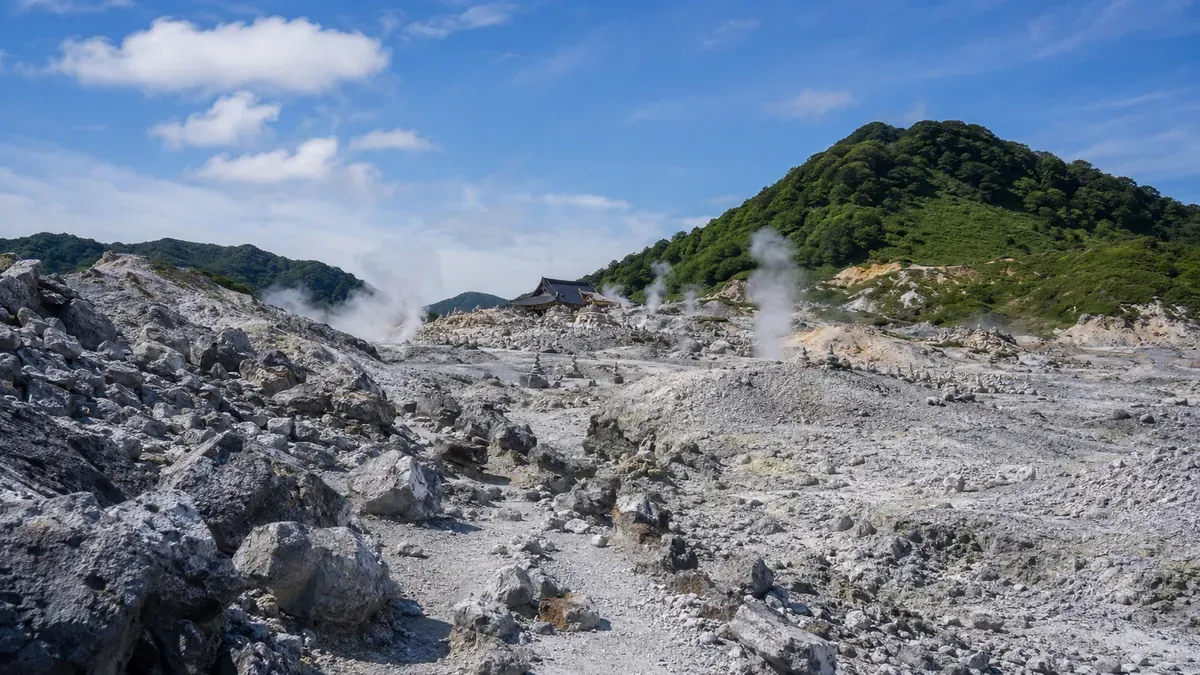 夏の青森県下北半島、恐山へ向かう山道の途中に広がる、硫黄の噴気が立ち上る荒涼とした大地