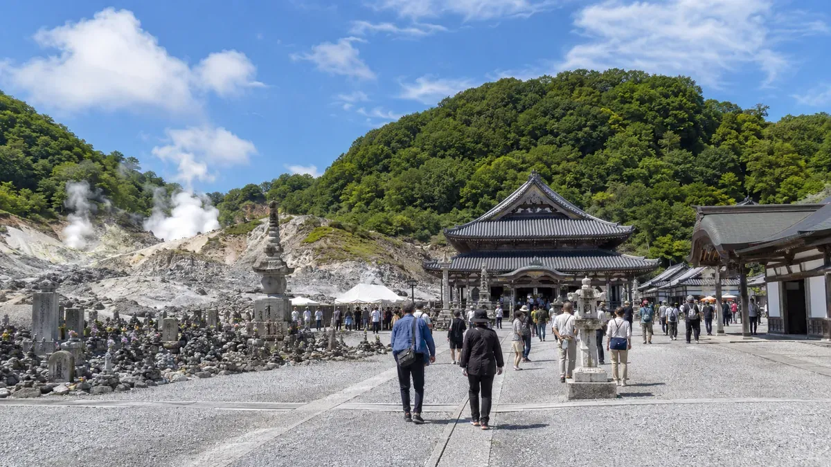 夏の青森県恐山菩提寺の山門前、石灯篭が並ぶ厳かな参道と古い山門