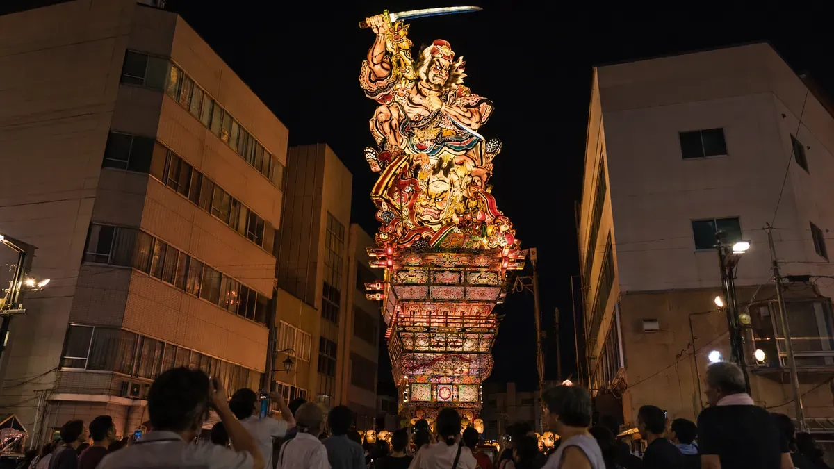 青森県五所川原市の夜、ビル街にそびえ立つ巨大な立佞武多を見上げる人々